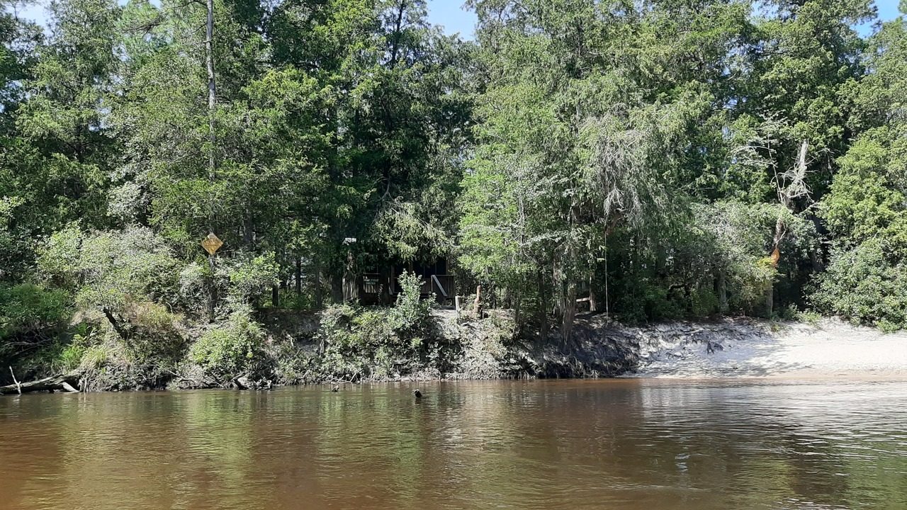 A wooden shelter tucked into the trees on the far bank of the river